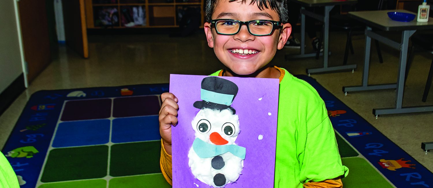 A young boy holds a photo of a snowman that he made himself