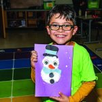 A young boy holds a photo of a snowman that he made himself