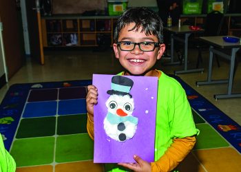 A young boy holds a photo of a snowman that he made himself